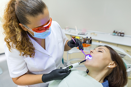 A dental hygienist performing oral care procedures on a patient, with the hygienist using an ultrasonic scaler.