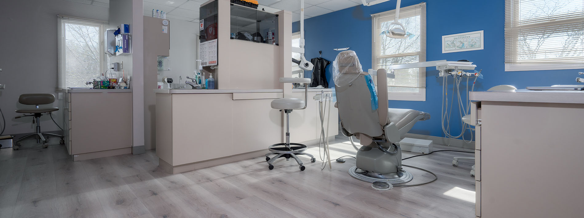 The image depicts a well-equipped dental office interior with various pieces of equipment and furniture typically found in such a setting, including chairs, a workstation, and cabinets.