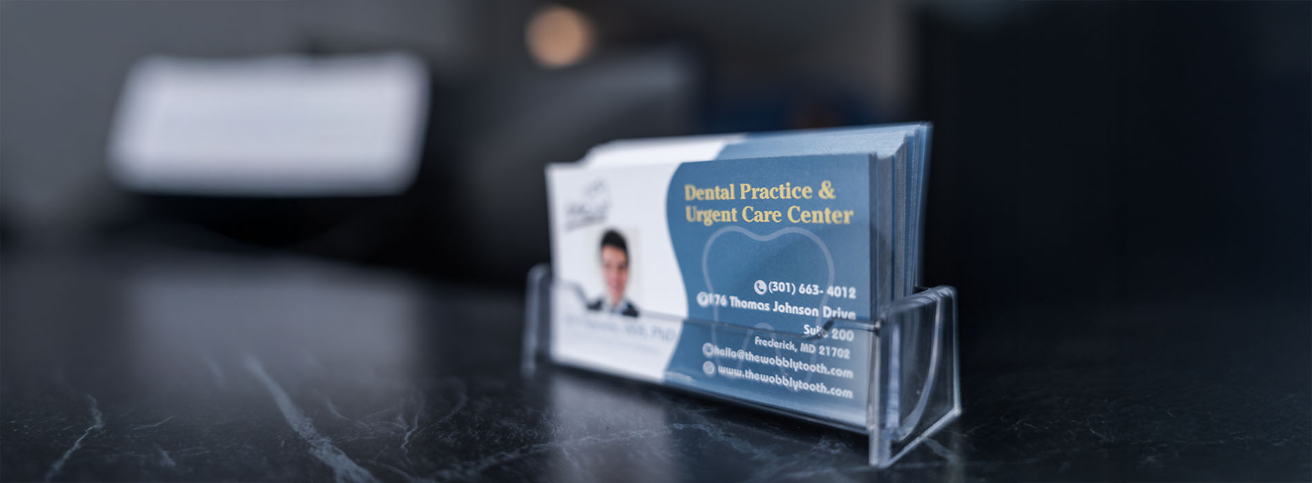 The image shows a business card holder with a single card displayed prominently, featuring text and contact information, placed on a surface with a blurred background.