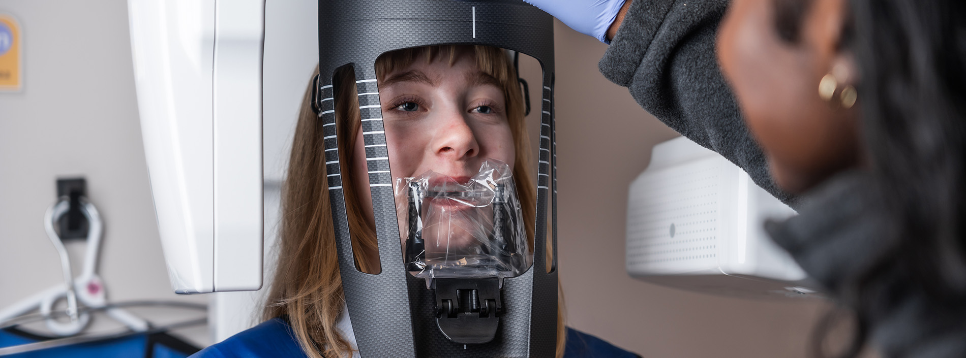 A person sitting in front of a dental mirror with a dental professional assisting them.
