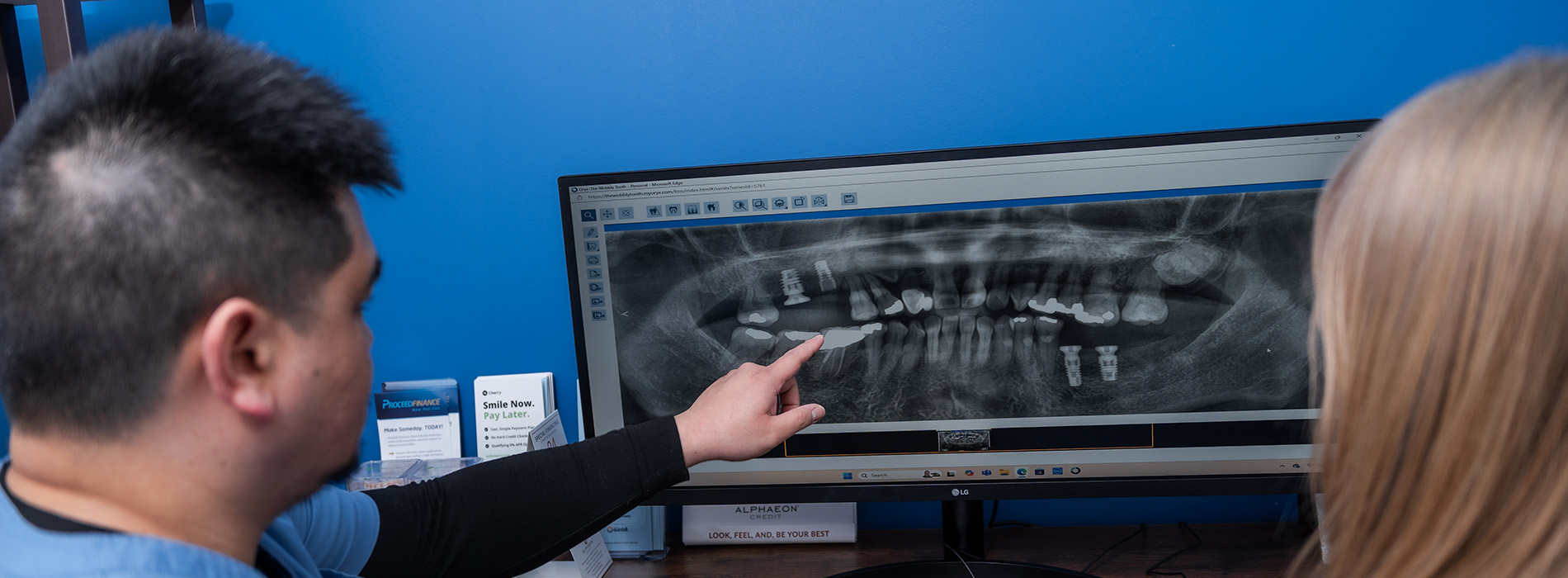 A person pointing at a dental X-ray on a computer screen while another looks on.