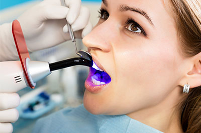 A woman receiving dental treatment, with a dentist using a device to clean her teeth while wearing protective gloves and a face mask.