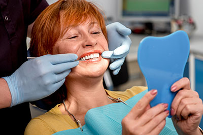 A woman with red hair sitting in a dental chair, smiling at the camera, while holding a blue dental mold with both hands.
