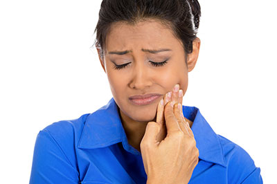 A woman with dark hair wearing a blue shirt, holding her chin with her right hand, and looking down with an expression of concern or worry.