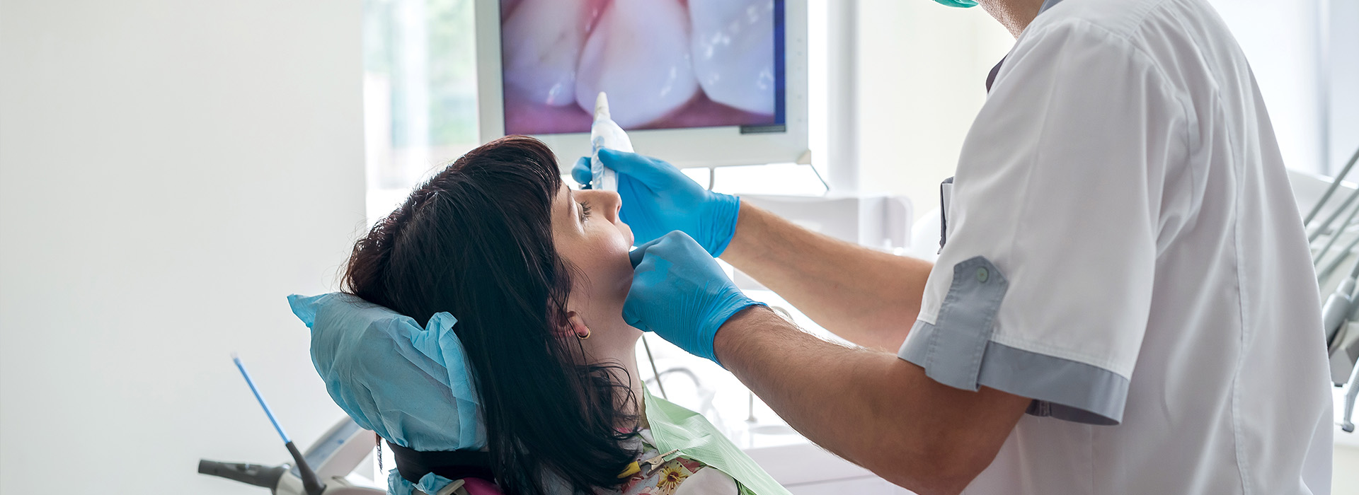 A dental hygienist cleaning a patient's teeth while wearing gloves and a mask.