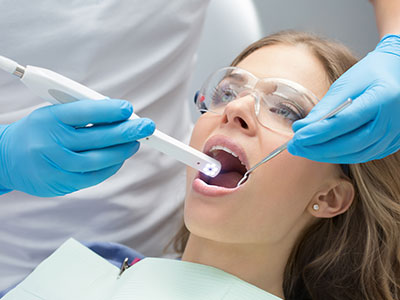A woman receiving dental care with a device held by a dental professional, who is wearing protective gloves and a face mask.